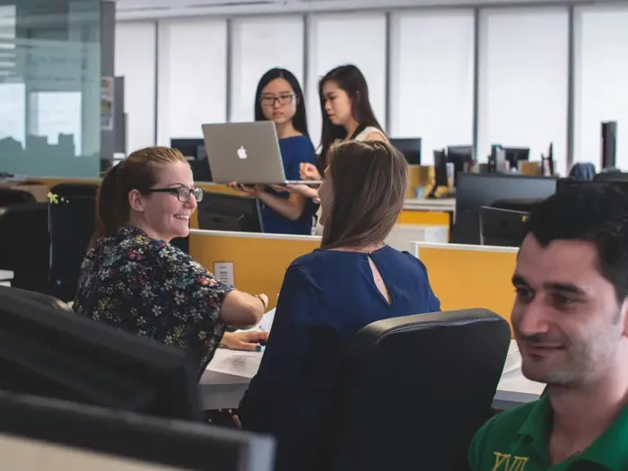 Smiling colleagues working together in a modern open office while two women discuss a project on a laptop